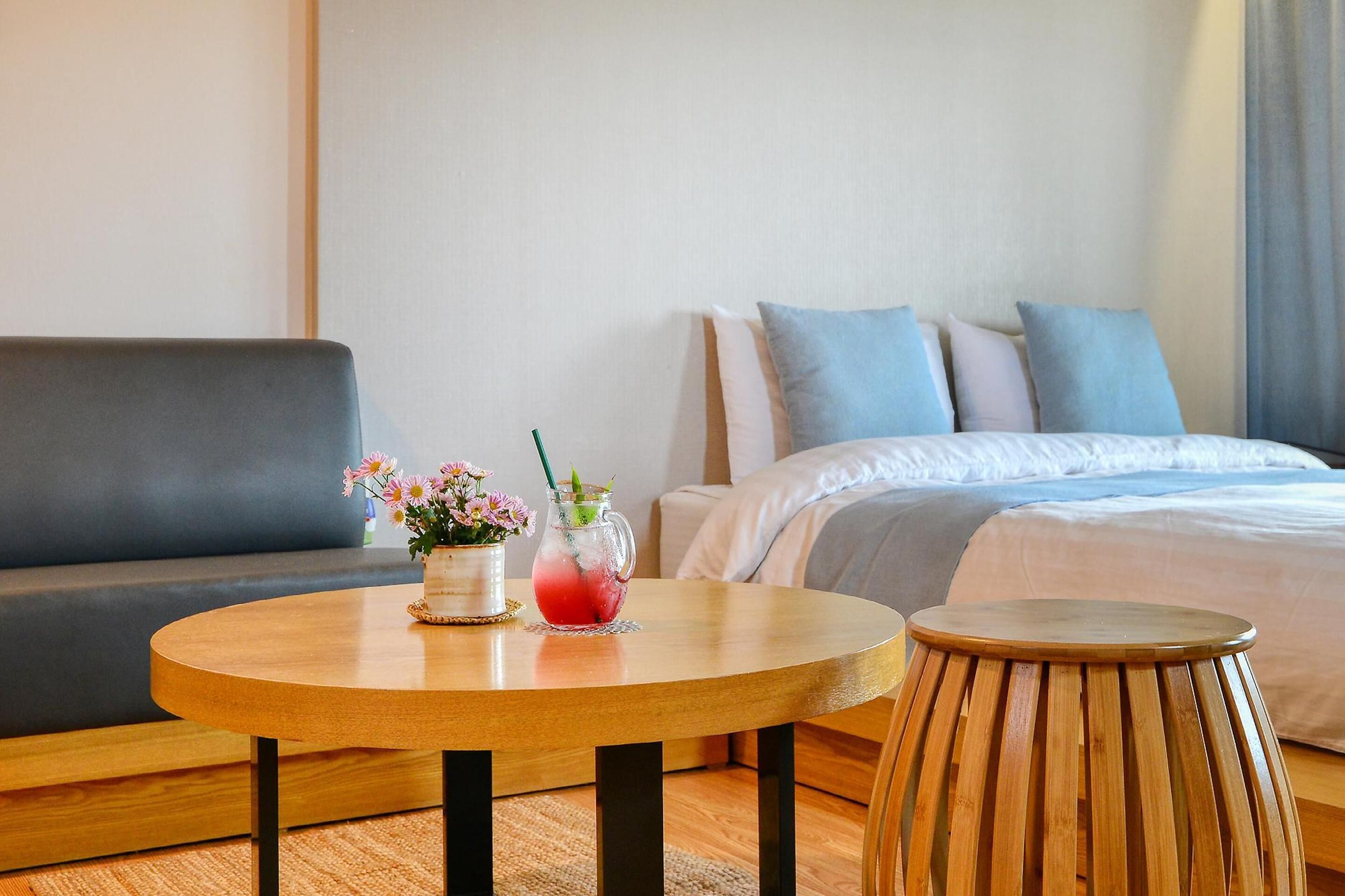 Quarto de hotel com cama, sofá, mesa de madeira redonda e um banquinho.
