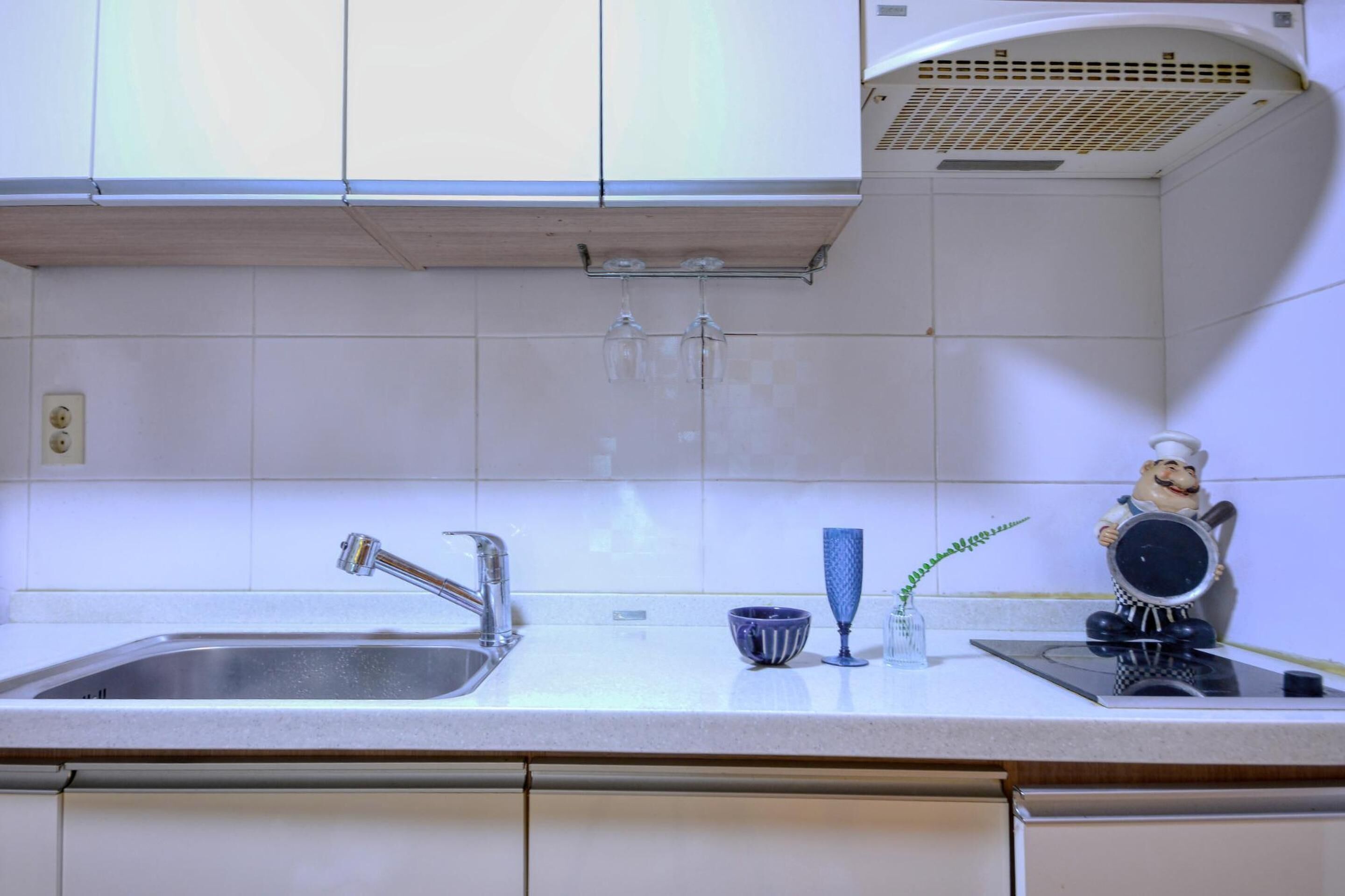 A kitchen with a stainless steel sink, a faucet, a blue glass, and a ceramic rooster figurine.
