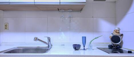 A kitchen with a stainless steel sink, a faucet, a blue glass, and a ceramic rooster figurine.