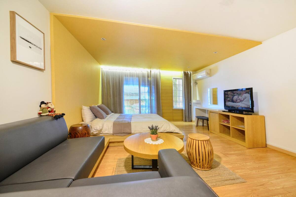 Una habitación de hotel moderna con una cama grande, un sofá, una mesa de centro de madera, un televisor y un mueble pequeño de madera.