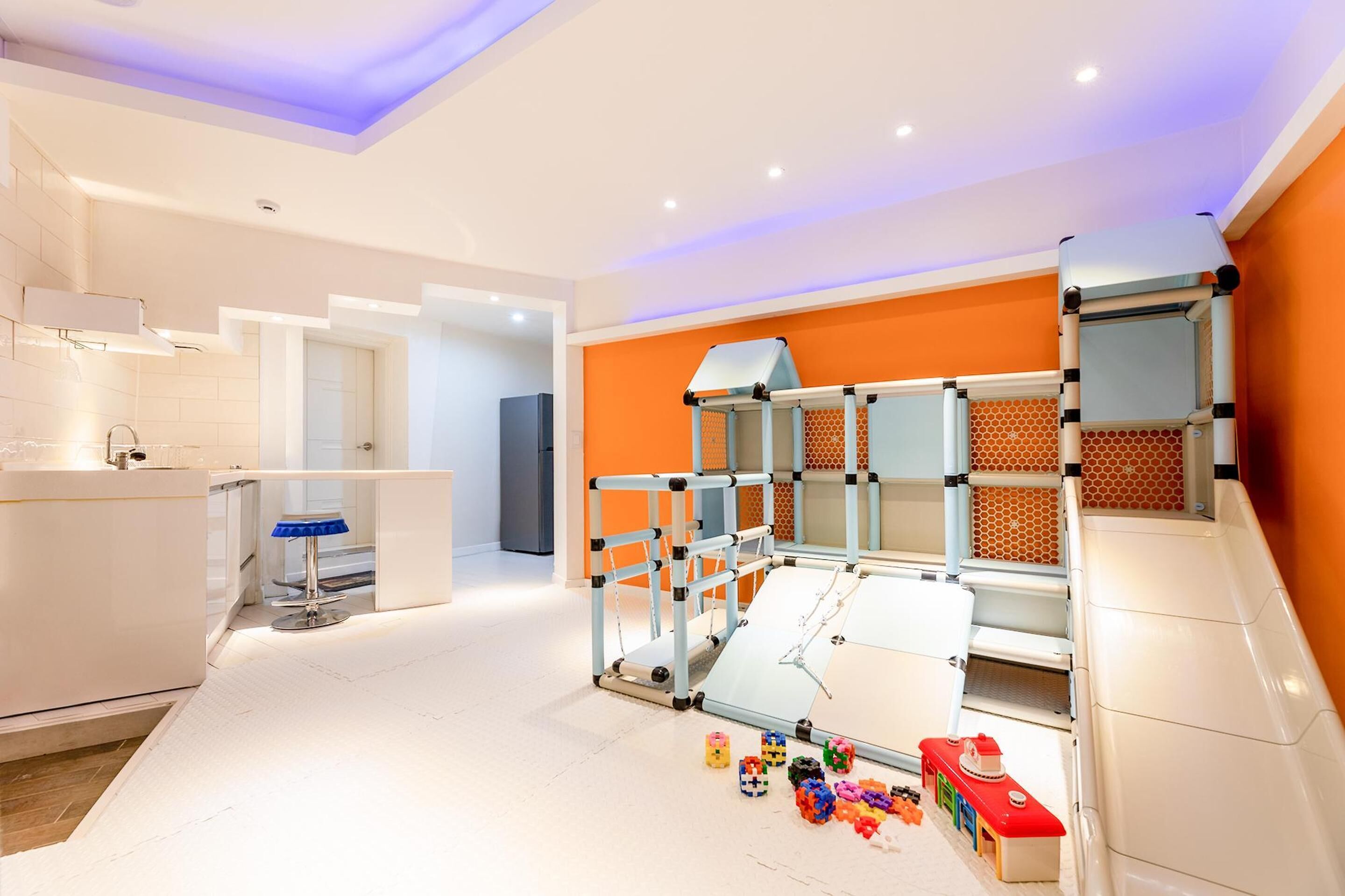 A modern, well-lit room with a large play area featuring a slide and climbing structure.