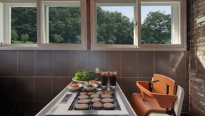Eine Küche mit Grill, einem Esstisch mit Speisen und Blick auf Bäume durch die Fenster.