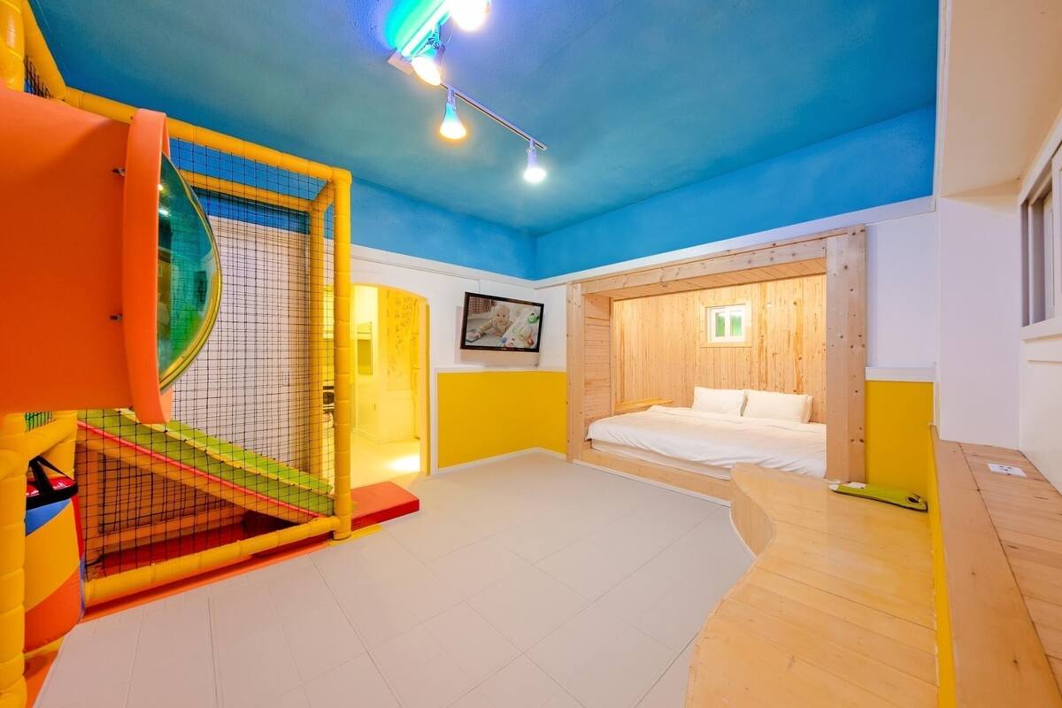 Ein Zimmer mit einem Bett, einem Spielbereich mit einer Rutsche und einer Holzwand.