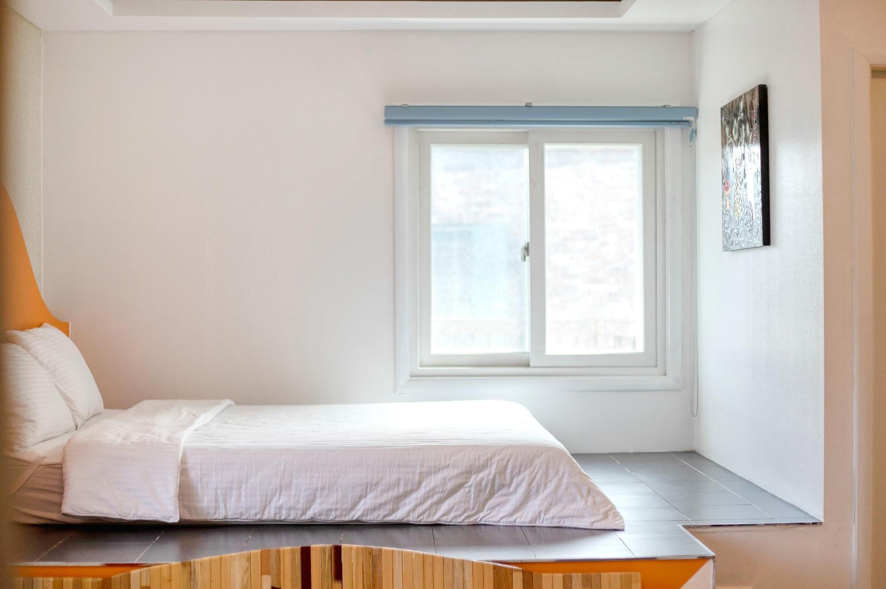A modern bedroom with a bed, a window, and a wall-mounted artwork.