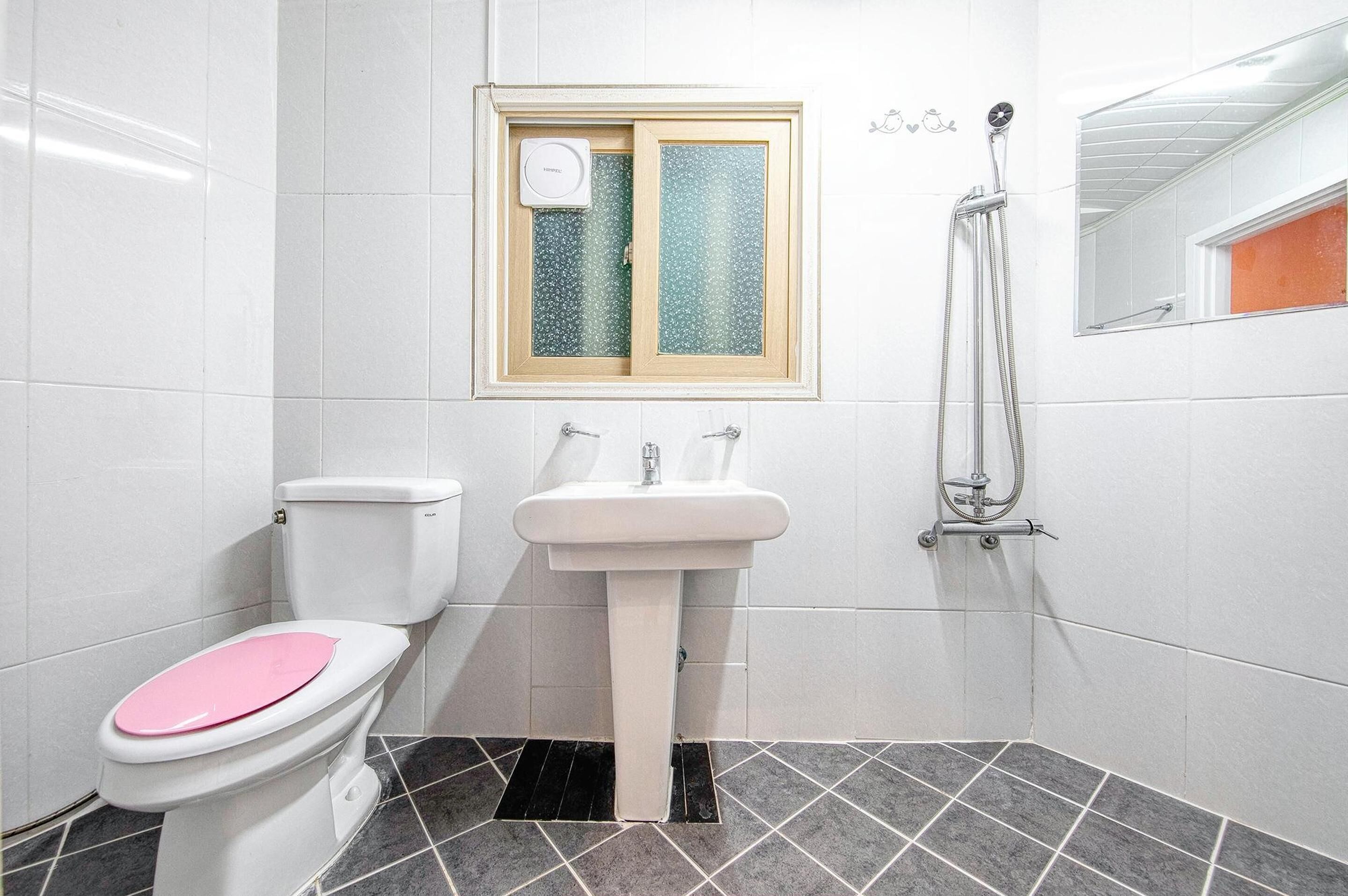 A bathroom with a toilet, sink, shower, and a window with frosted glass.