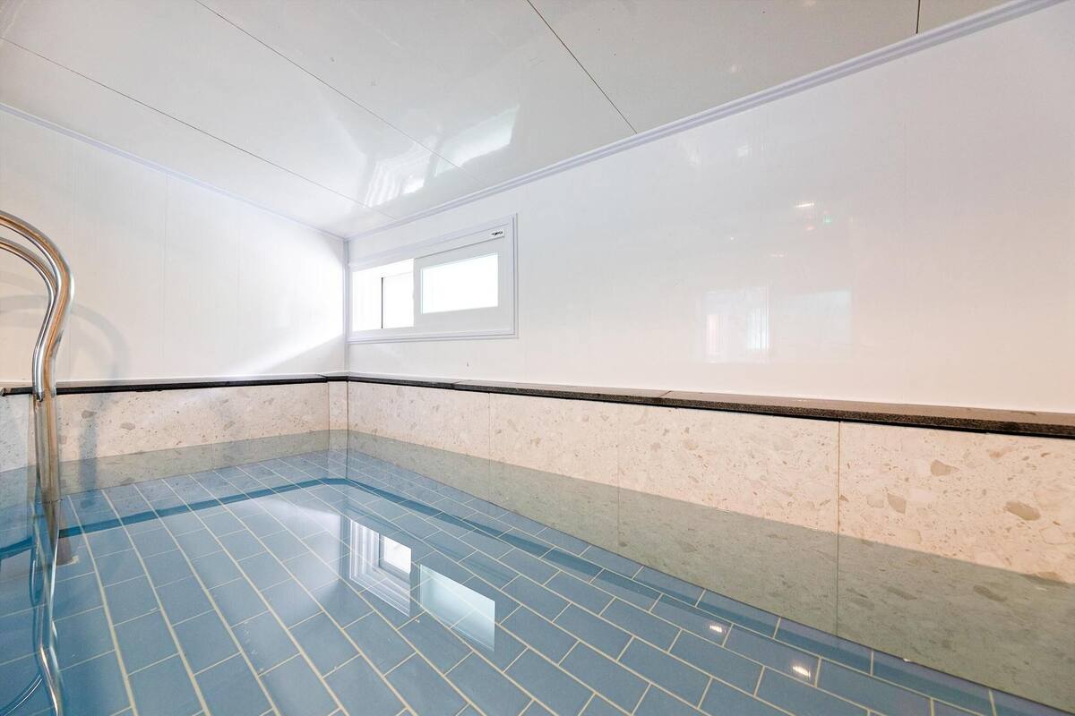 Ein Schwimmbecken mit blauen Fliesen, einem Metallhandlauf und einer Wand mit einem Fenster.