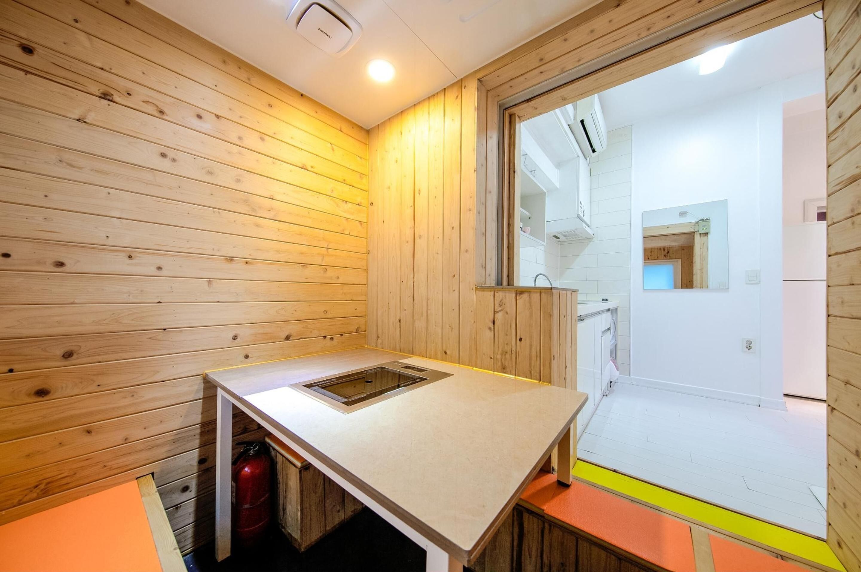 A small, compact kitchen with wooden walls, a built-in sink, and a window overlooking a white interior space.