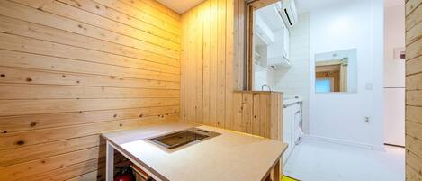 Una cocina pequeña y funcional con paredes de madera, un lavamanos empotrado y una ventana que da a un espacio interior blanco.