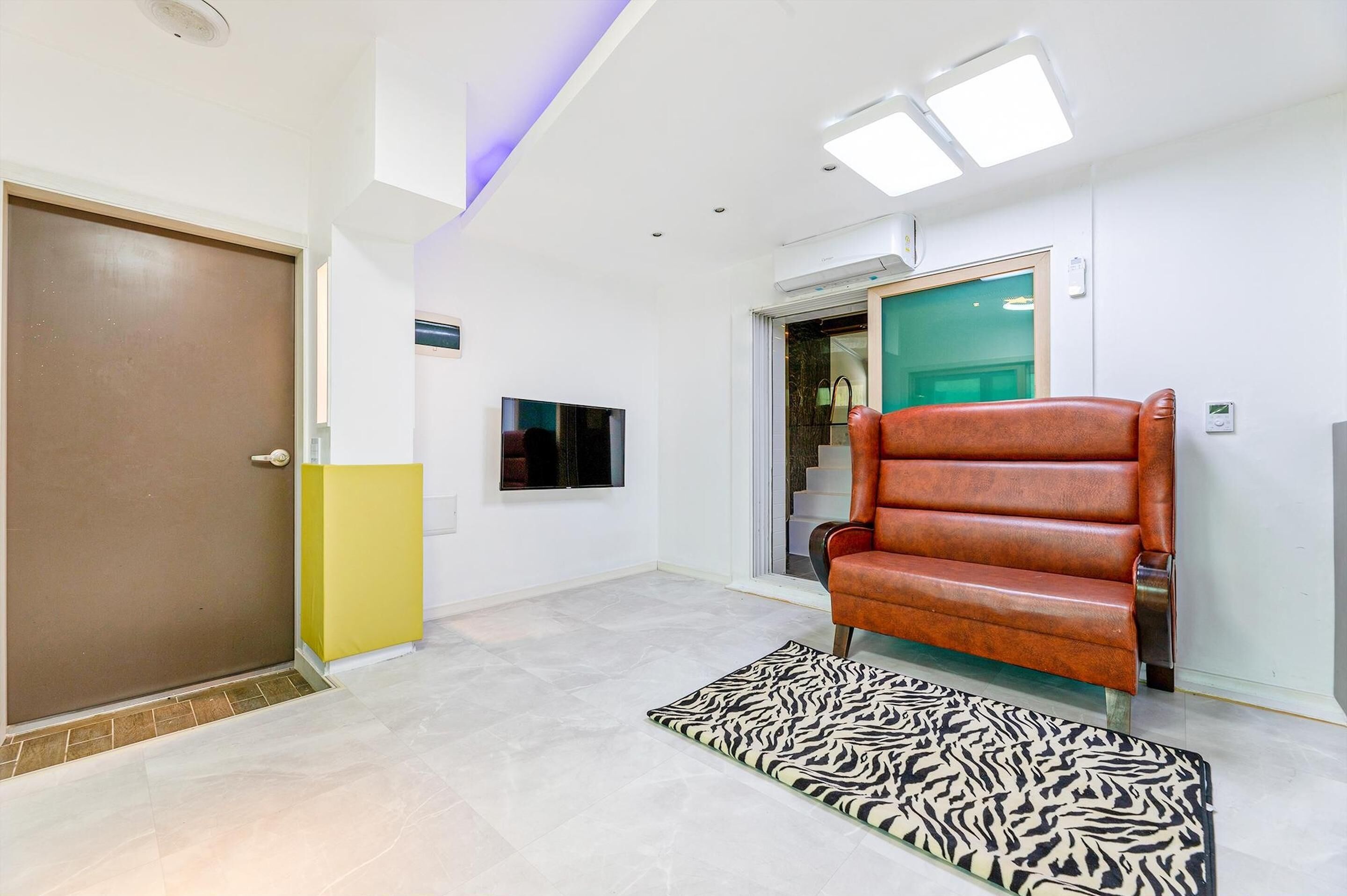 Un couloir moderne avec une porte marron, un meuble jaune, un tapis à motifs zébrés et un fauteuil en cuir.