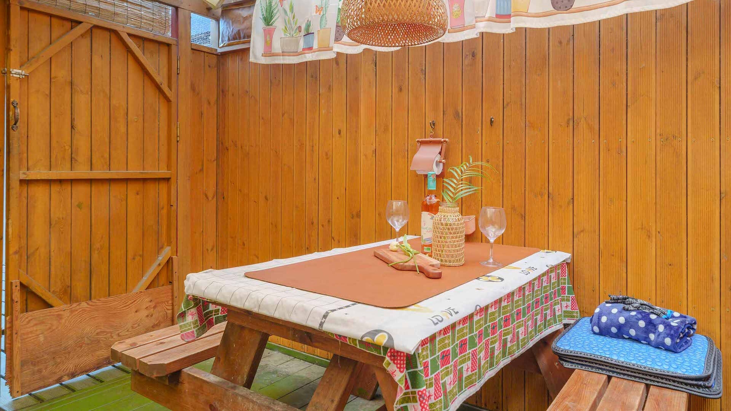 Una terraza de madera con una mesa para dos, un banco y una maceta colgante.