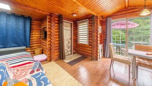 A log cabin interior with a bed, a table, and a view of greenery outside. - Pocheon Arumdri Pension (Pocheon)