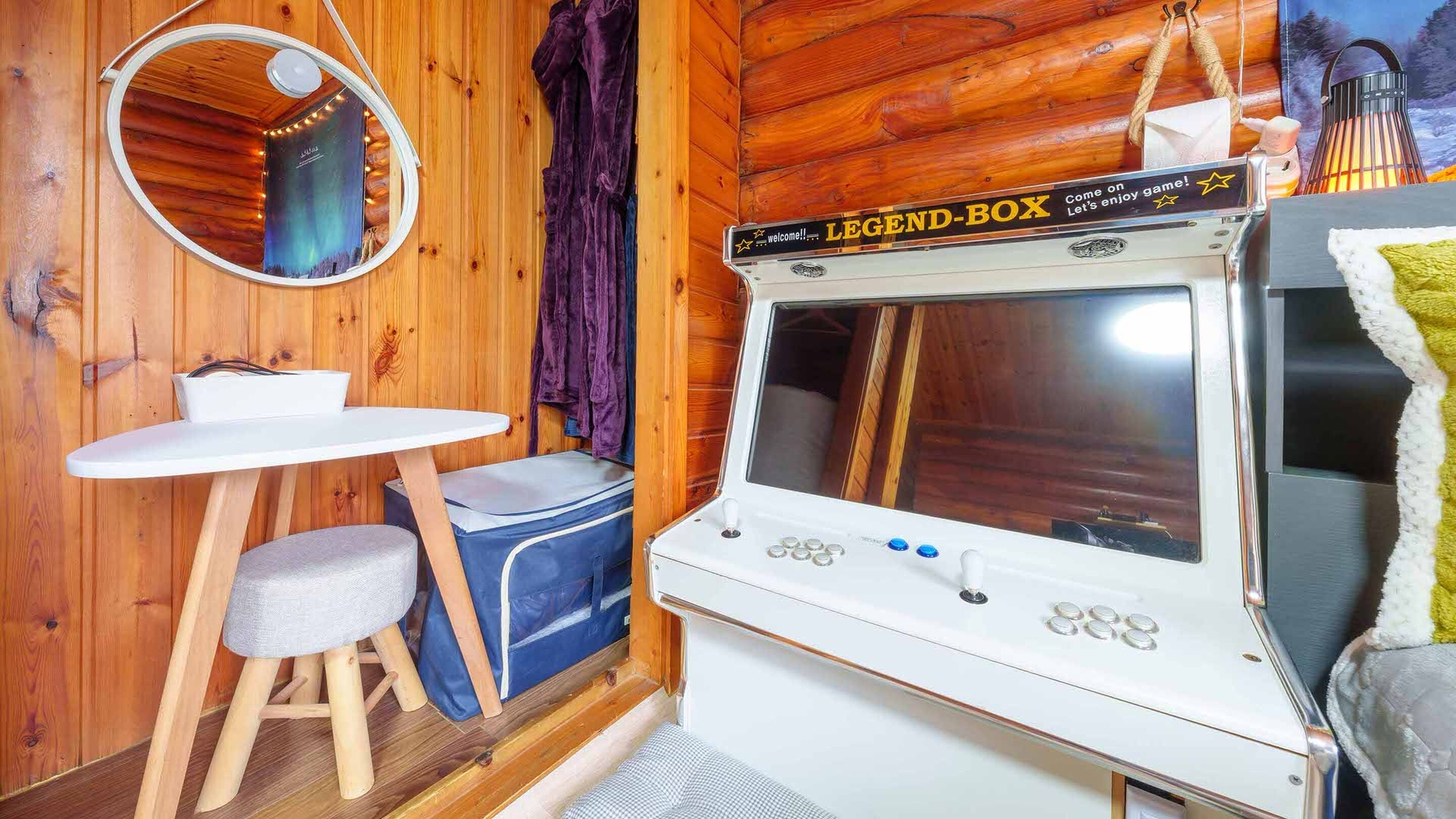 Ett mysigt rum med träinredning, ett litet bord med en stol, en bänk, en spegel och en tv som är märkt med texten "LEGEND-BOX".