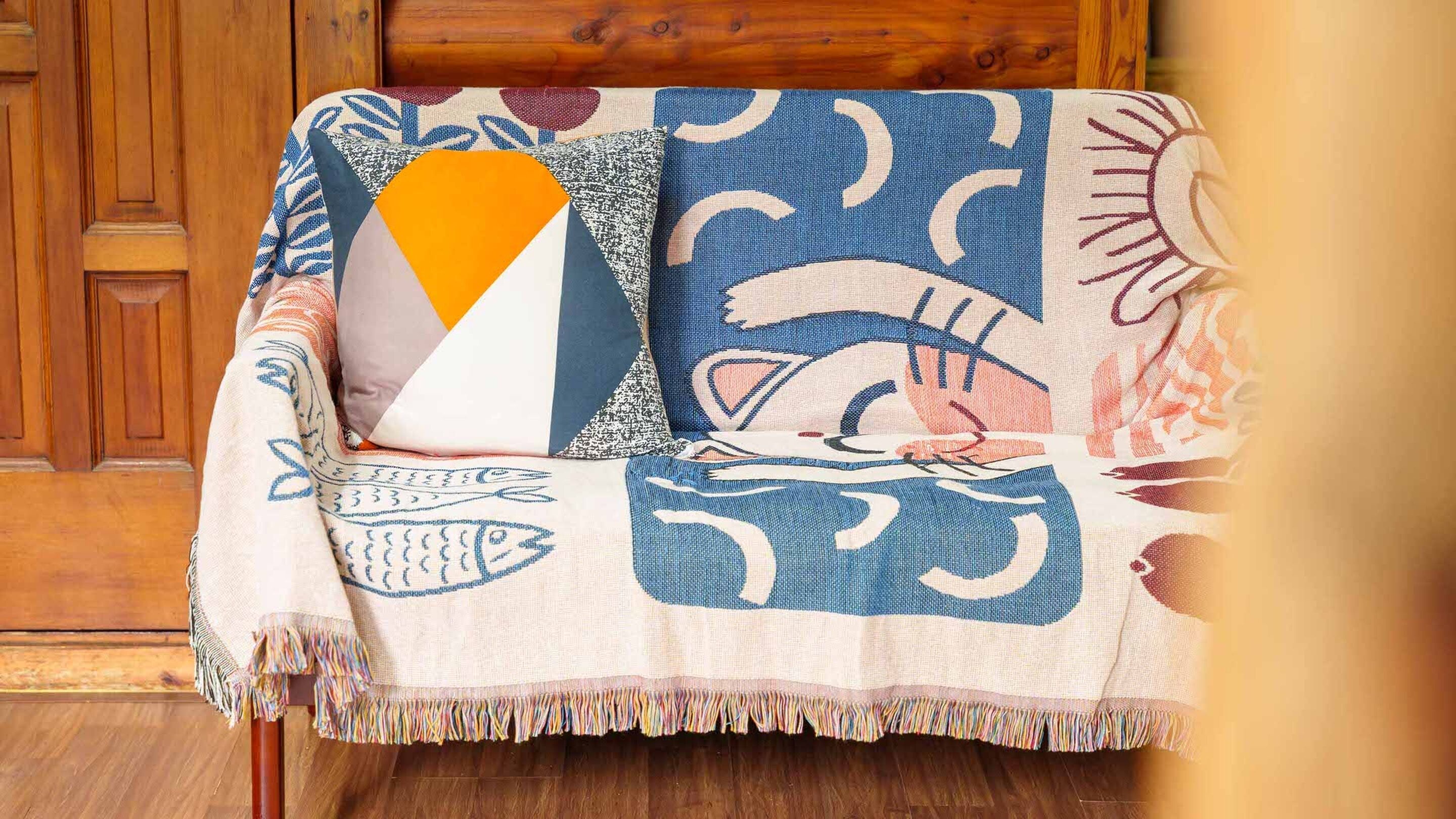 A wooden chair with a colorful blanket featuring geometric patterns and a fringe.