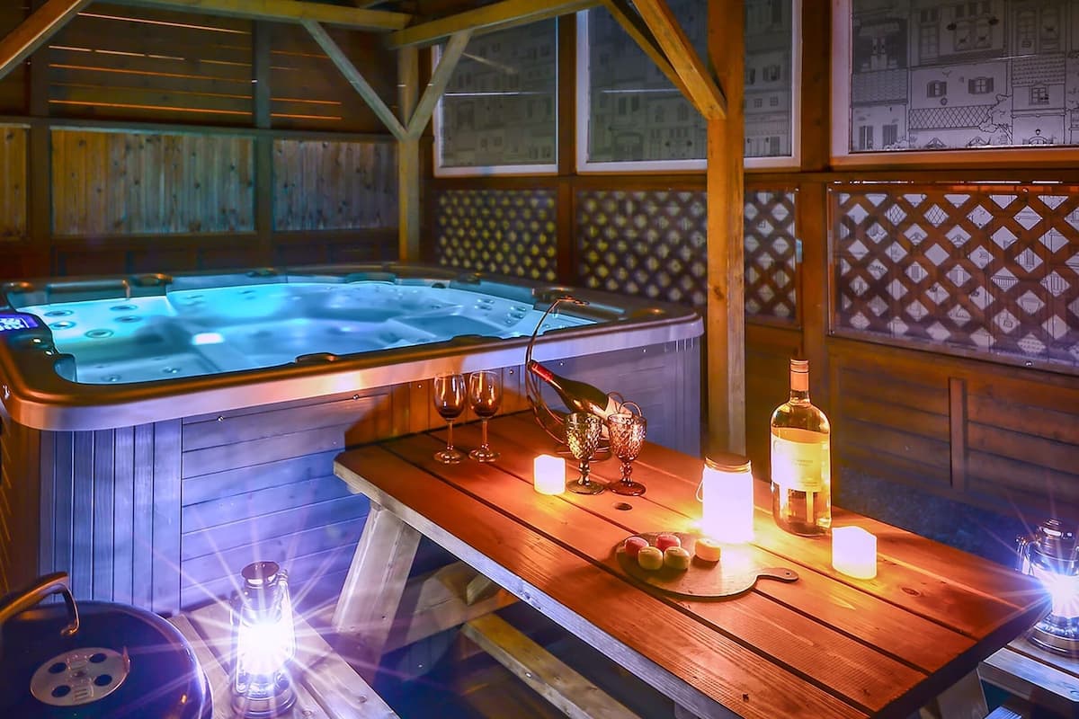 Uma cabana de madeira com hidromassagem, uma mesa com velas e um candeeiro.
