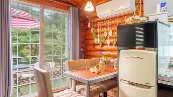 A cozy cabin-style room with a wooden interior, a dining table with chairs, a refrigerator, and a large window with curtains. - Pocheon Arumdri Pension (Pocheon)