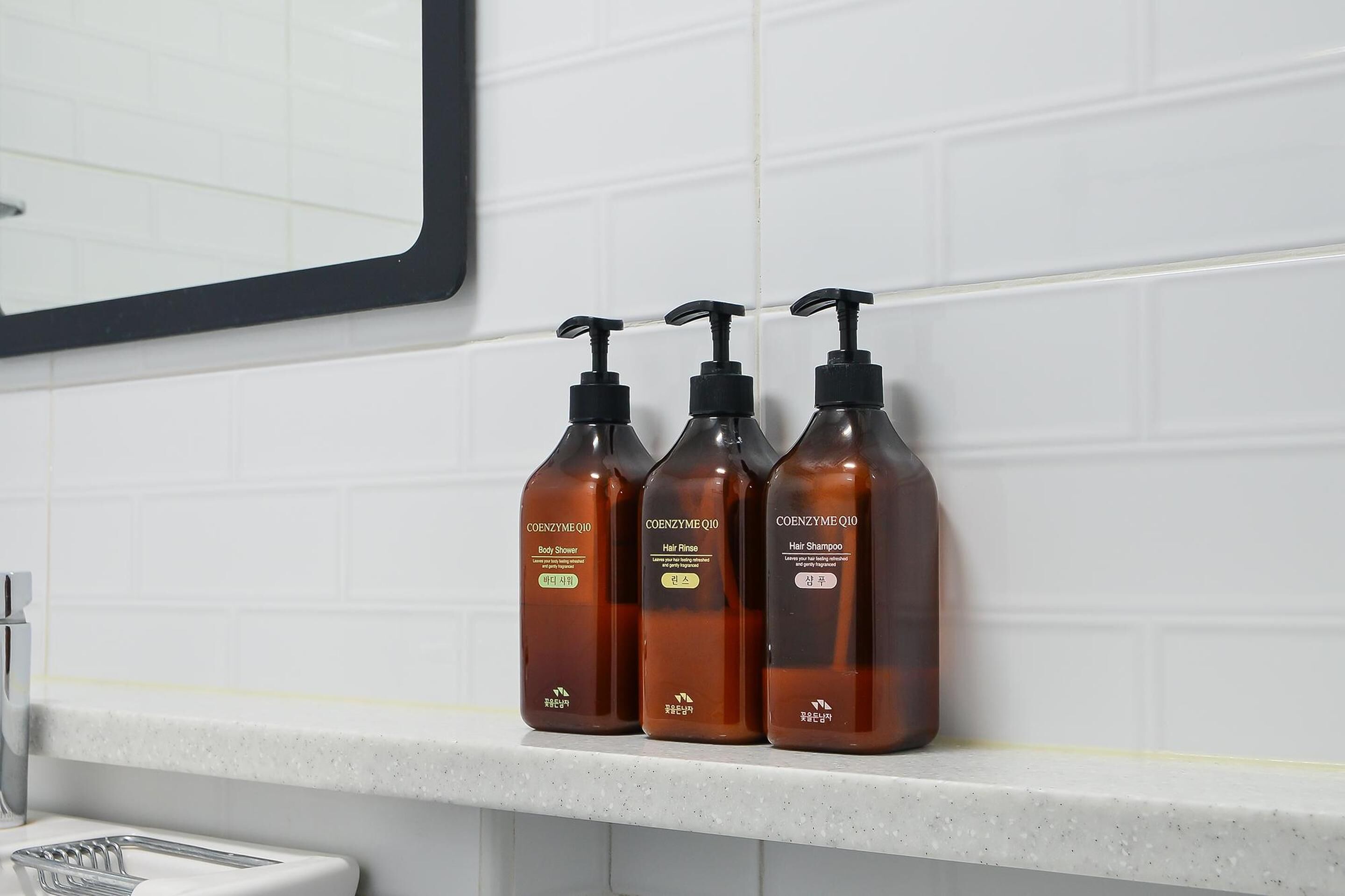 Tres botellas marrones de Coenzyme Q10: acondicionador, champú y enjuague corporal, sobre una encimera blanca.