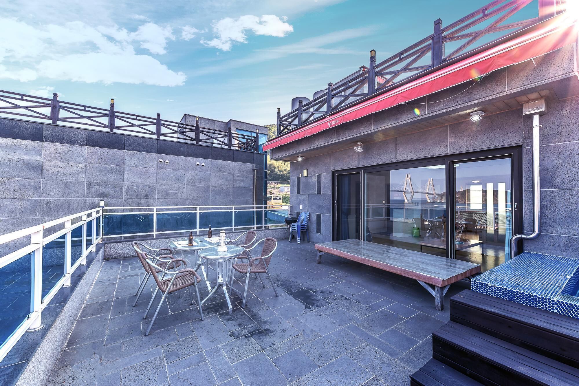 An outdoor patio with a table and chairs, a glass-enclosed area with seating, and a view of a bridge in the background.