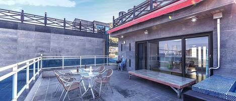 An outdoor patio with a table and chairs, a glass-enclosed area with seating, and a view of a bridge in the background.