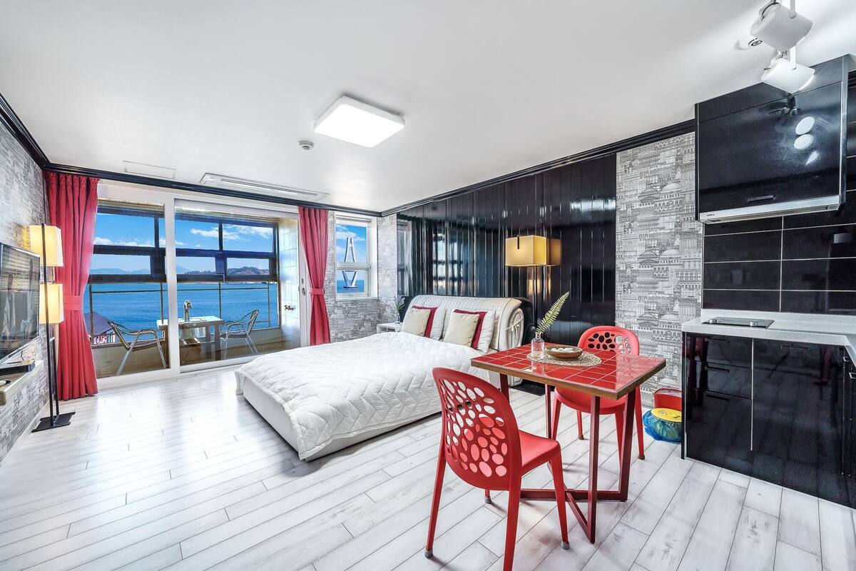 A modern bedroom with a large bed, a dining table, and a view of the sea.