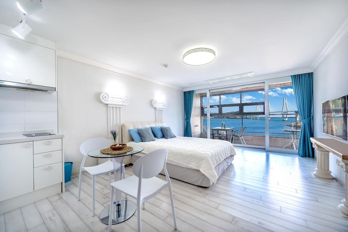 A modern hotel room with a balcony, a dining area, and a bed with a view of a bridge.