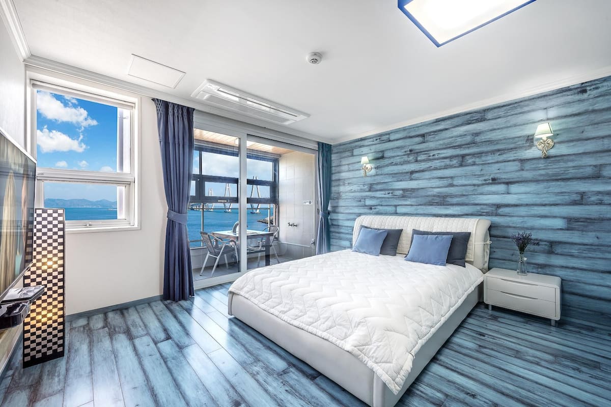 A bedroom with a large bed, a nightstand, a window with a view of a bridge, and a checkered table runner.