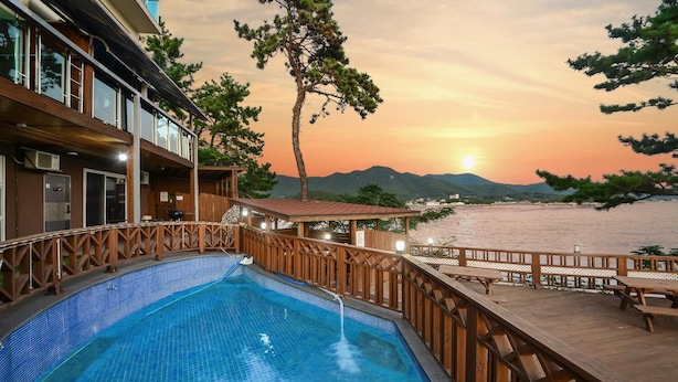 A swimming pool with a wooden deck and a view of the sunset over a body of water. - Tongyoung Seychelles Poolvilla (Tongyeong)