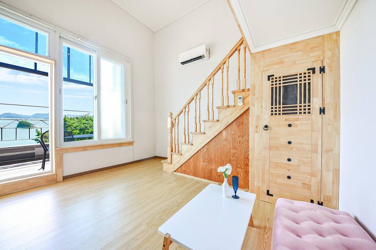 Ein modernes Zimmer mit einer Holztreppe, einem weißen Tisch mit einer Vase und Blick ins Freie.