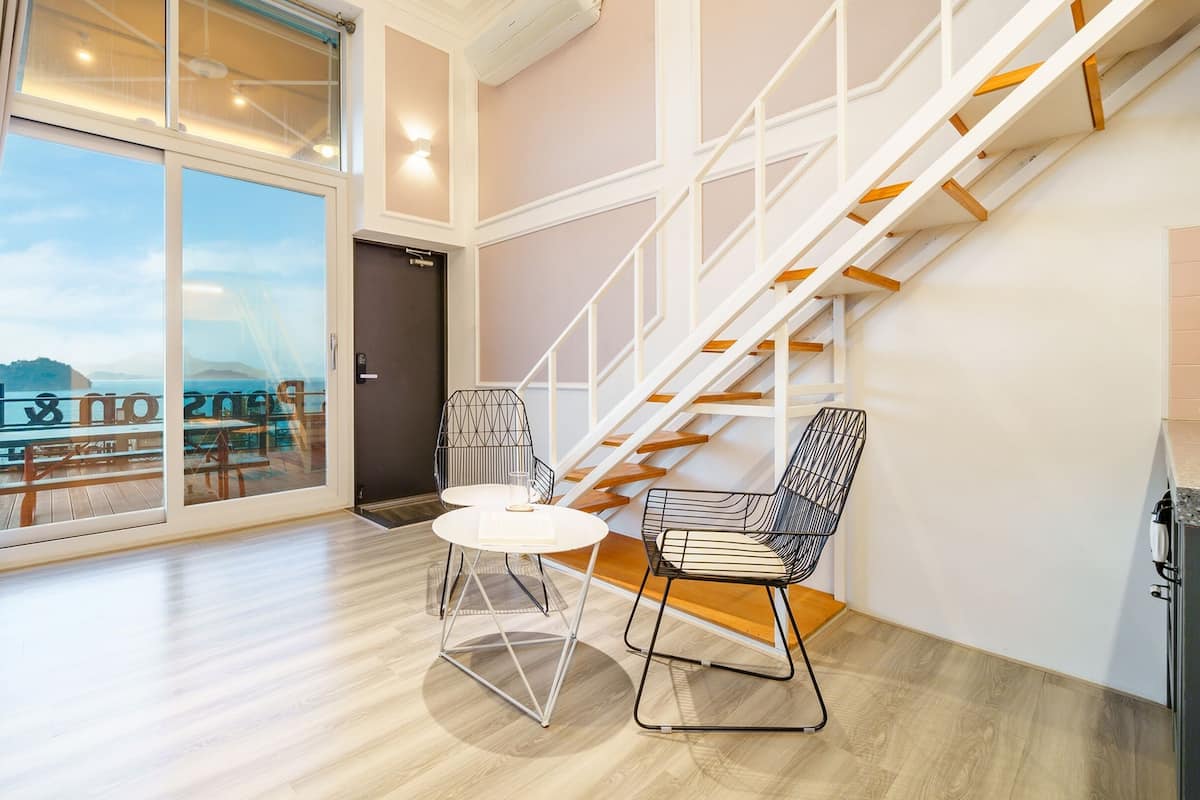Ein modernes Hotelzimmer mit einer großen Schiebeglasdoor, die auf einen Balkon führt, einer Treppe und zwei modernen Sesseln.