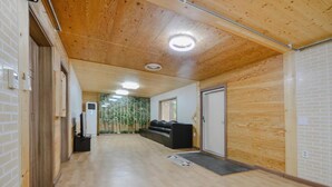 A hallway with wooden flooring and walls, a black sofa, and a door. - Yangyang Water Sol Valley Pension (Yangyang)