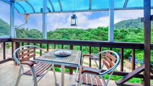 A covered outdoor seating area with a table and chairs, overlooking a lush green landscape. - Yangyang Water Sol Valley Pension (Yangyang)