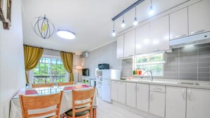 A modern kitchen with white cabinets, a dining table with chairs, and a large window with curtains. - Yangyang Water Sol Valley Pension (Yangyang)