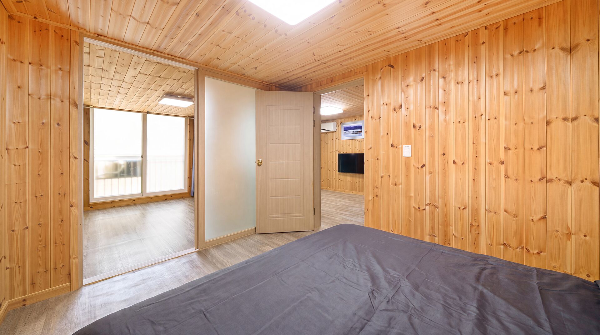 Una habitación con paredes de madera, una cama, una puerta que da a un balcón y un televisor en la pared.