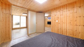 Una habitación con paredes de madera, una cama, una puerta que da a un balcón y un televisor en la pared.