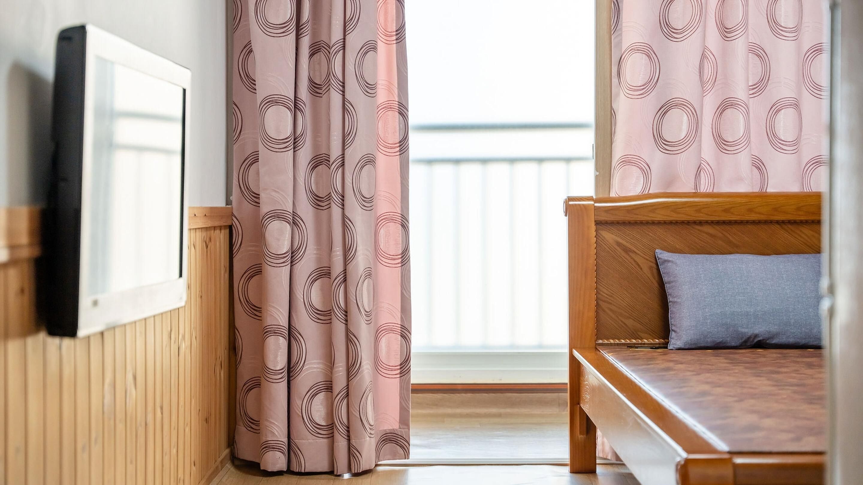 Une chambre à coucher avec un lit en bois, un oreiller gris et une fenêtre ornée de rideaux roses.