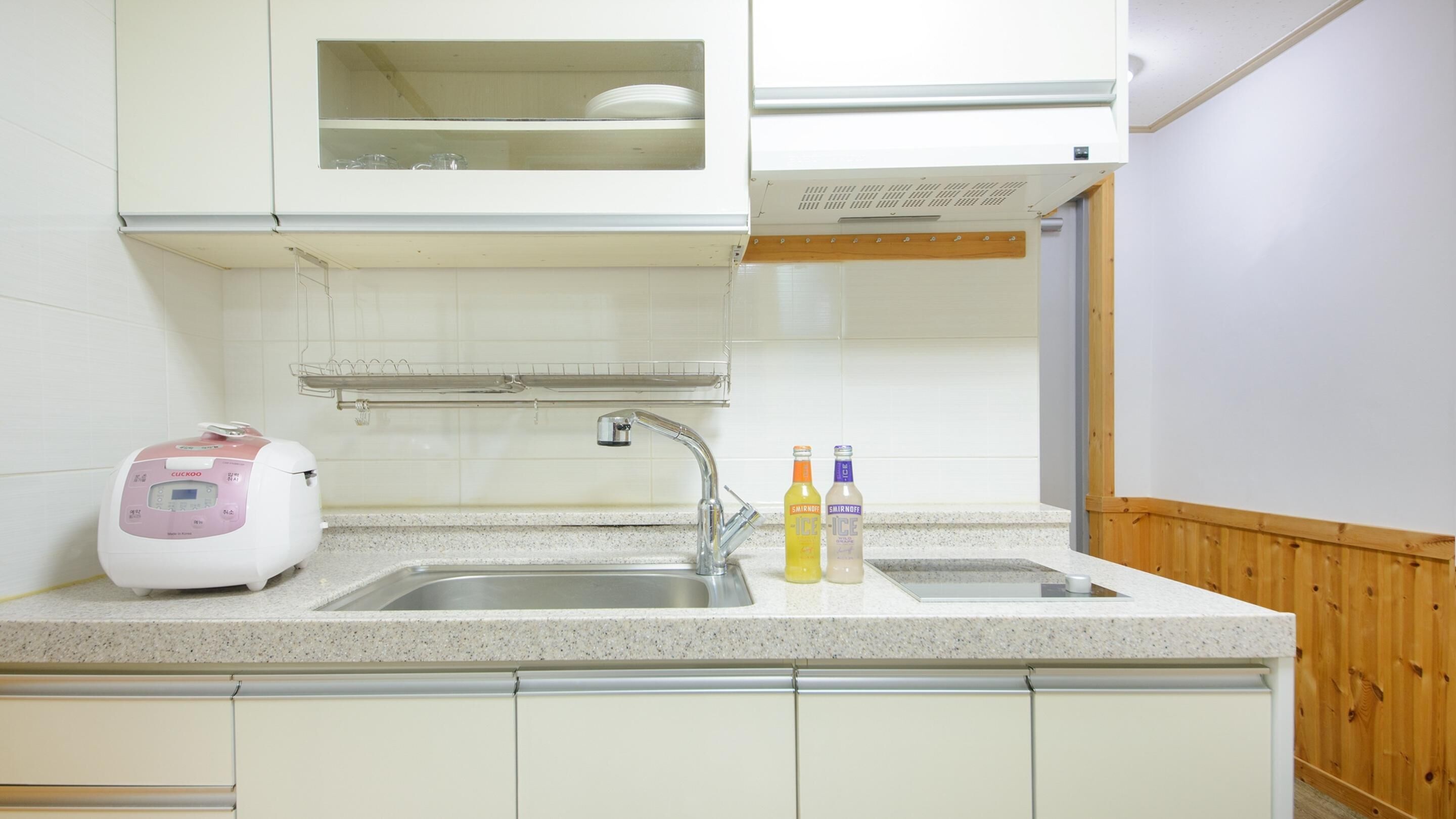 Uma cozinha com máquina de lavar louça embutida, pia de aço inoxidável e duas garrafas de Smirnoff Ice no balcão.