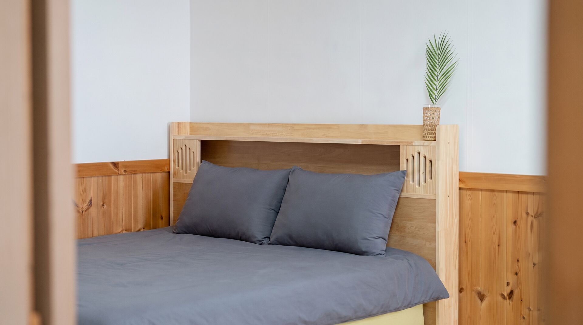 A wooden bed with two pillows and a plant on the headboard.