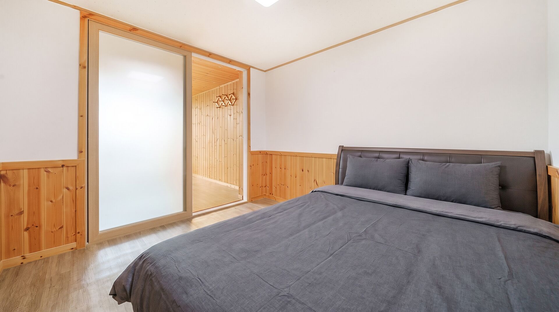 A bedroom with a bed, wooden walls, and a sliding door.