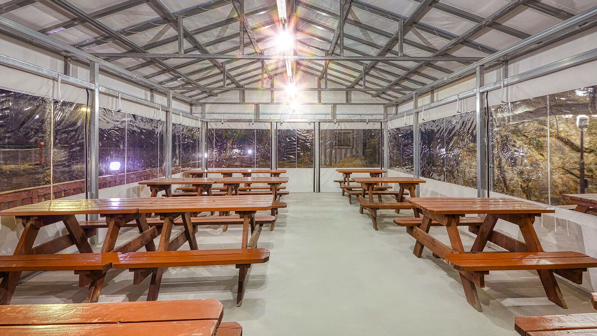 A covered outdoor dining area with picnic tables and large windows.