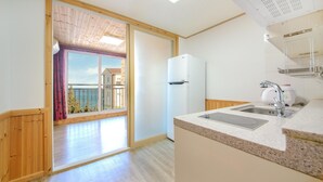 A kitchen with a built-in oven, a sink, and a view of a balcony with a wooden railing. - Samcheok sky Pension (Samcheok)