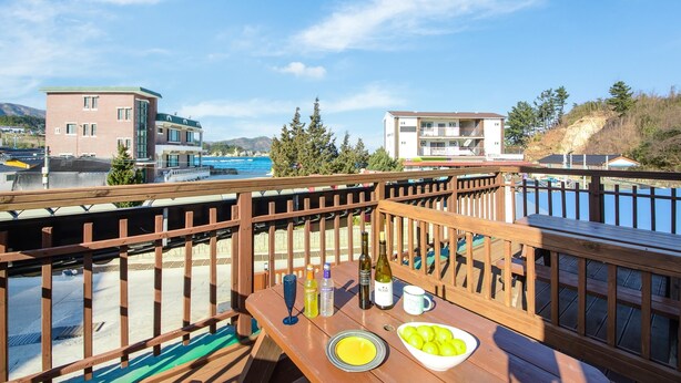 A wooden deck with a table set for a meal, overlooking a body of water and buildings. - Samcheok sky Pension (Samcheok)
