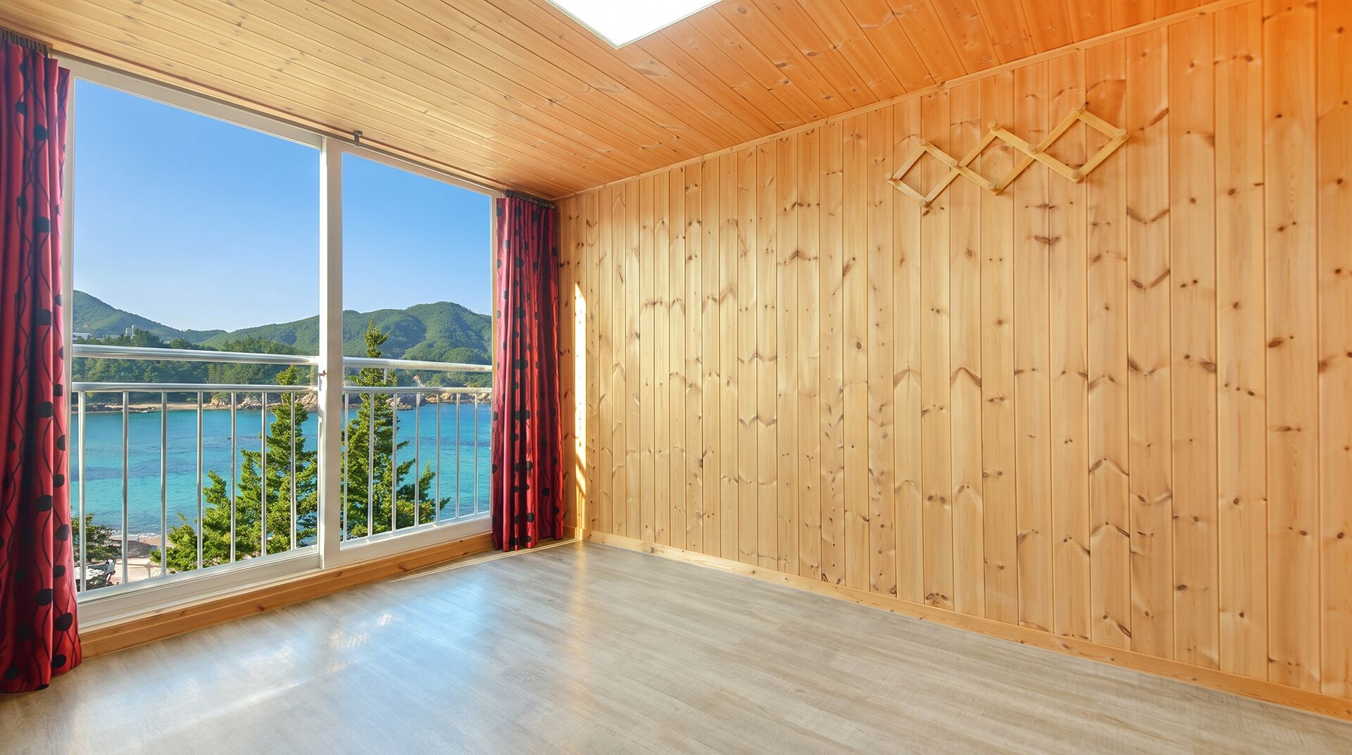 Una habitación con paredes de madera, un ventanal con cortinas y vistas a un cuerpo de agua y colinas.