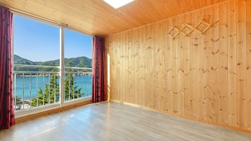 Una habitación con paredes de madera, un ventanal con cortinas y vistas a un cuerpo de agua y colinas.