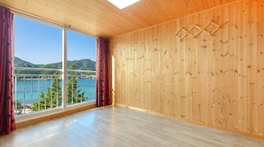 Una habitación con paredes de madera, un ventanal con cortinas y vistas a un cuerpo de agua y colinas.