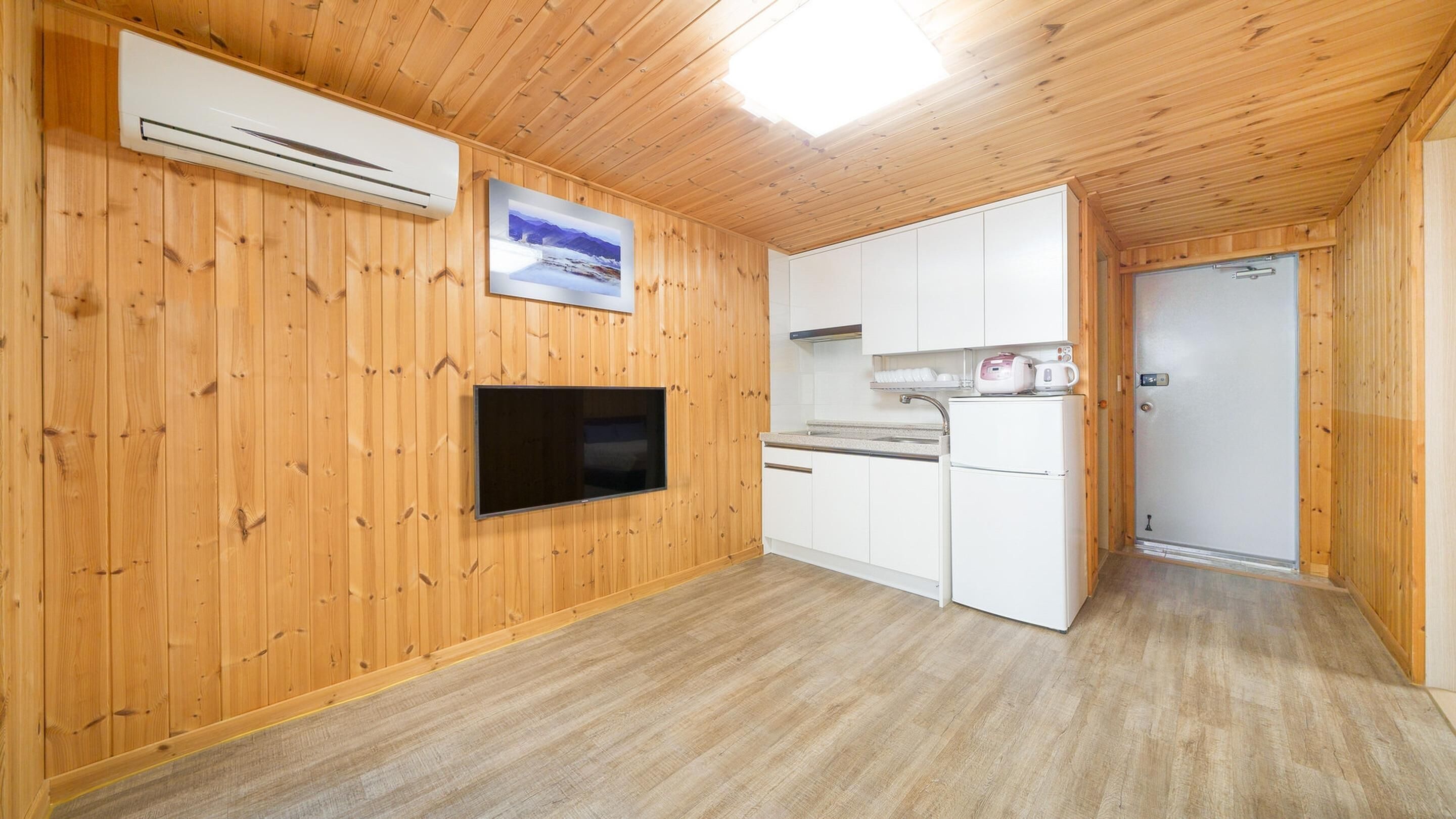 Una cuina compacta amb parets de fusta, un televisor de pantalla plana i un refrigerador.