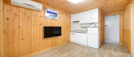 Una cuina compacta amb parets de fusta, un televisor de pantalla plana i un refrigerador.