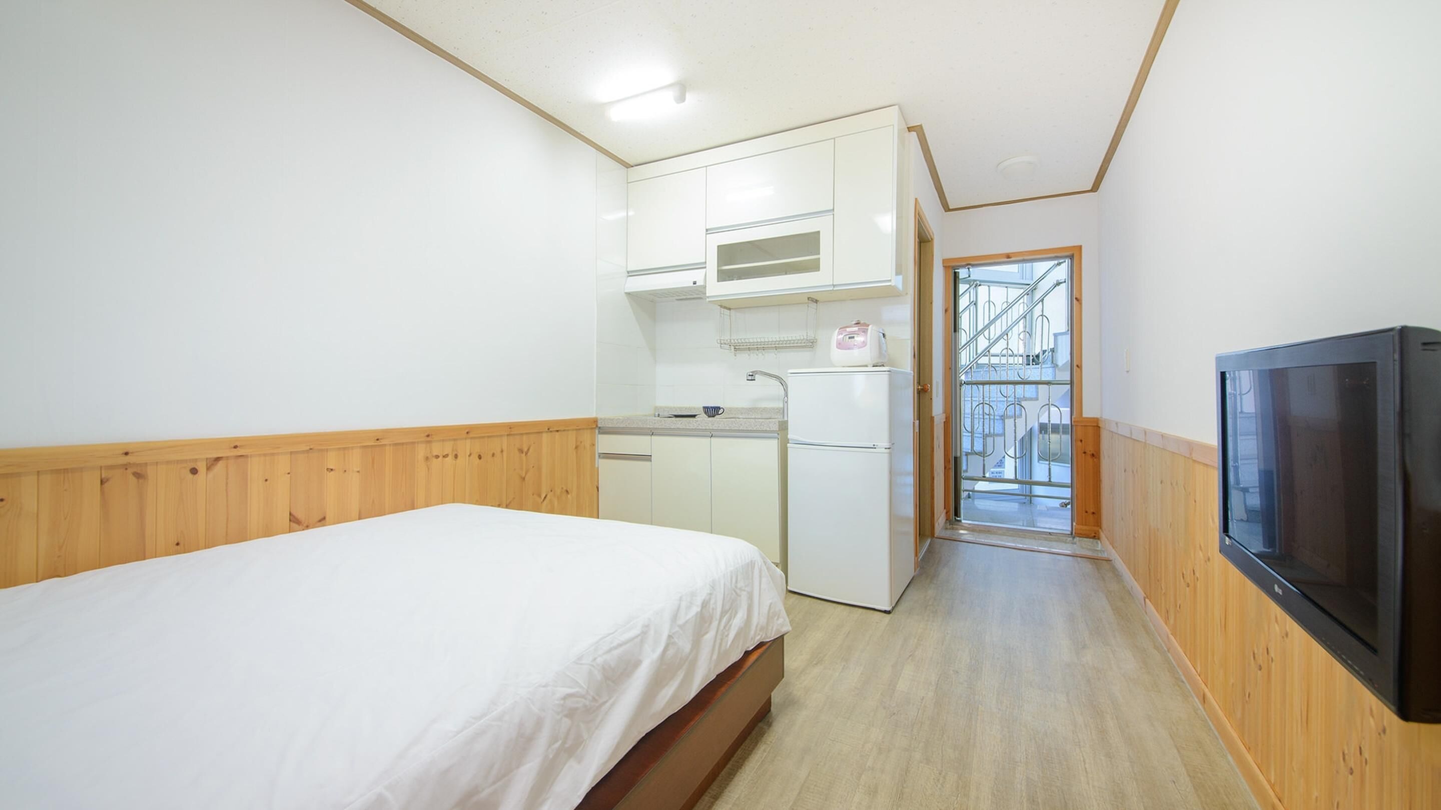 A compact room with a bed, kitchenette, and a TV.