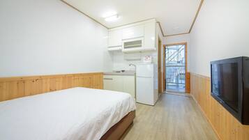A compact room with a bed, kitchenette, and a TV.