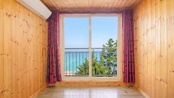 Una habitación con paredes de madera y un amplio ventanal corredera que da a un balcón con vistas al mar.