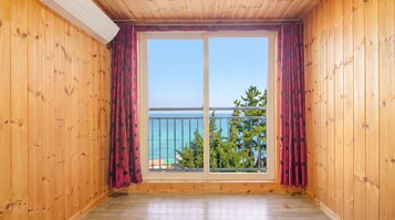 A room with wooden walls and a large sliding glass door leading to a balcony with a view of the sea.