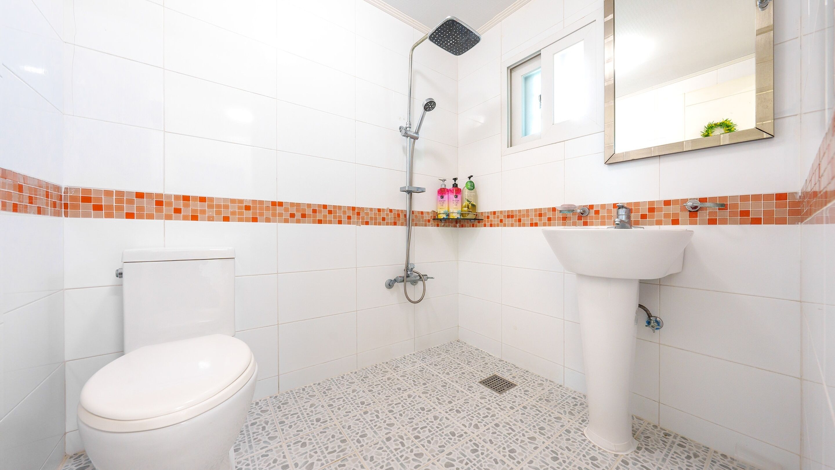 A bathroom with a toilet, a shower, a sink, and a mirror.